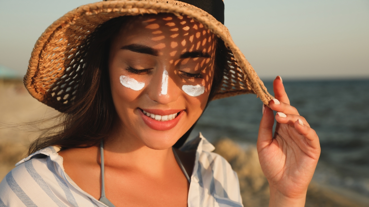 Žena sa SPF kremom na licu sedi na plaži tokom sunčanog dana