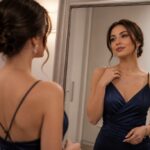 Žena u tamnoplavoj haljini sa V-izrezom pred ogledalom proverava kako joj stoje srebrna ogrlica i minđuše.