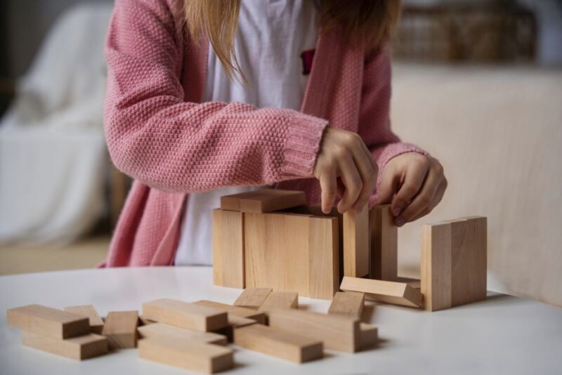 Dete slaže drvene kocke na stolu tokom kreativne igre